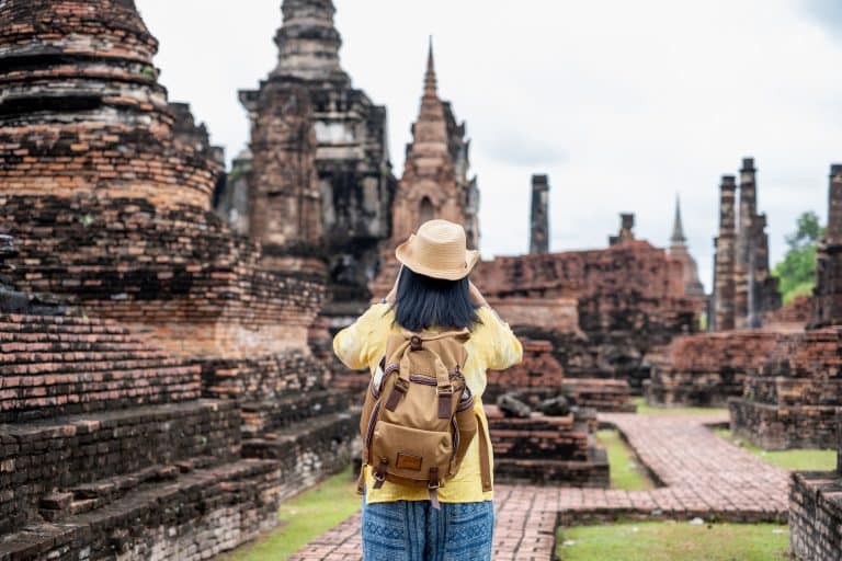 Asian tourist woman take a photo of ancient of pagoda temple thai architecture at Sukhothai Historical Park,Thailand. Female traveler in casual thai cloths style visiting city concept
