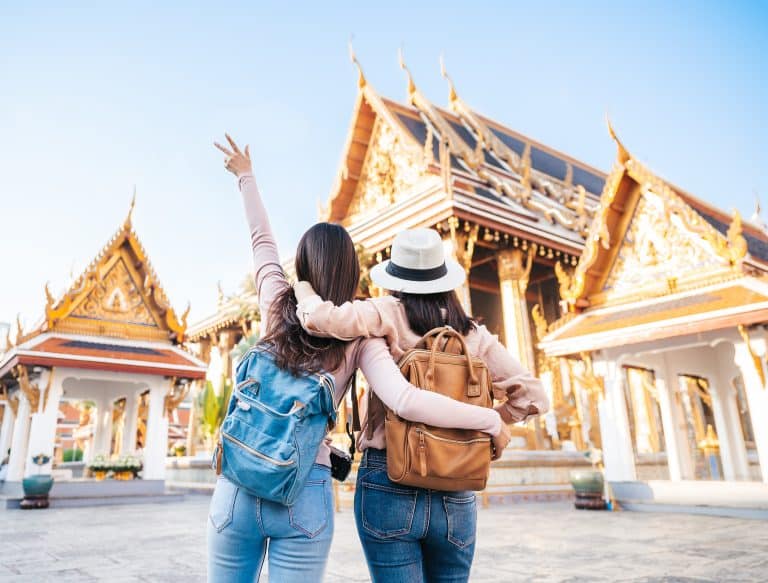Rear view of two Asian women traveller best friends having fun during vacation in teple of the emerald buddha in Thailand